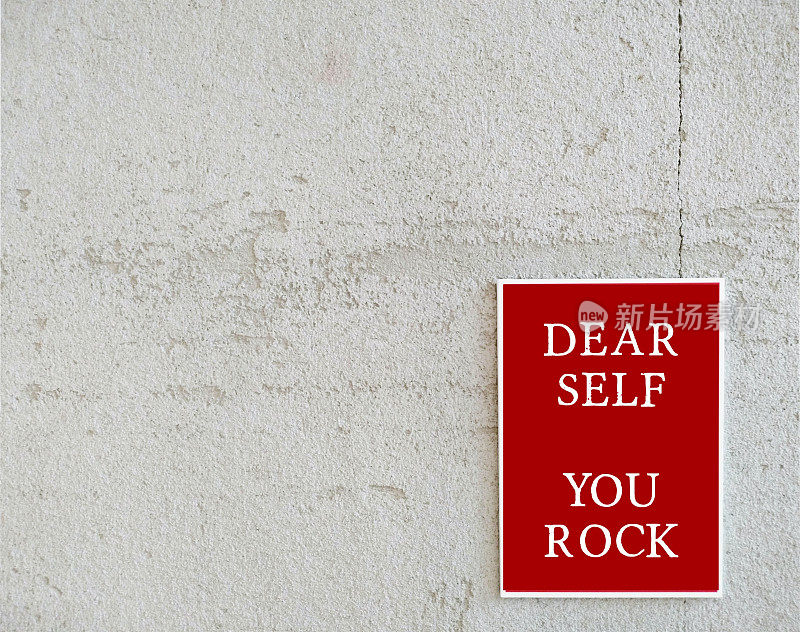 复制空间白墙上的红色海报上写着“DEAR SELF YOU ROCK”的文字，积极的自我对话提高自尊的概念，日常美好的肯定提醒力量和克服困难的能力